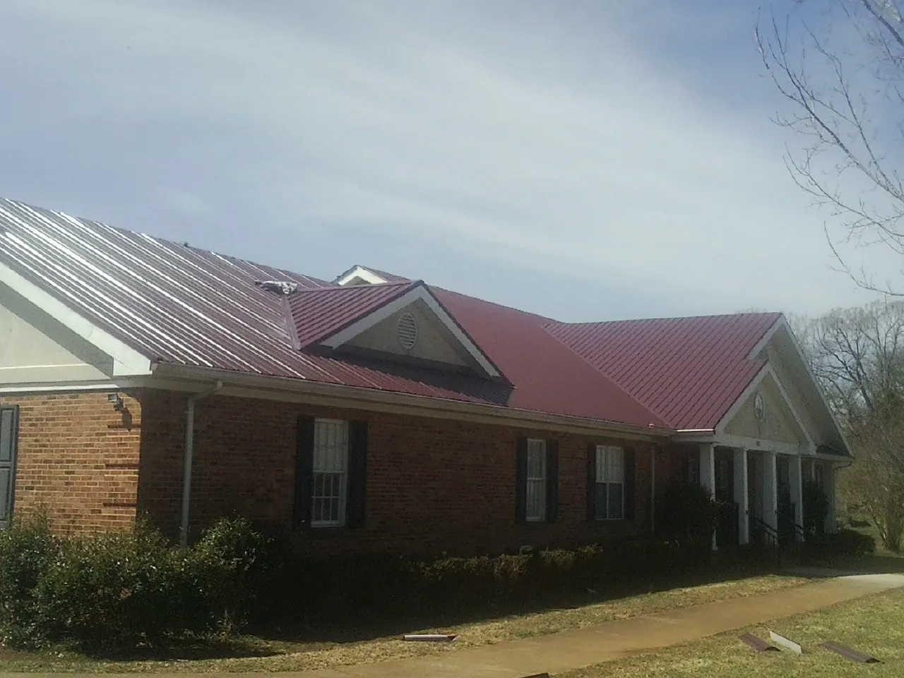 Red metal roof with gabled entries on a long brick building, from a Hail Damage Roof Repair job in Laredo