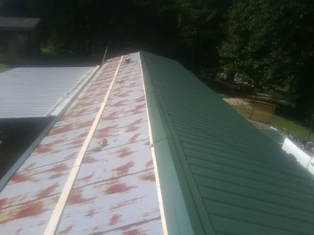 Old rusted panels beside newly installed green metal roofing — Wind Damage Roof Repair by Roofing Brothers in Laredo